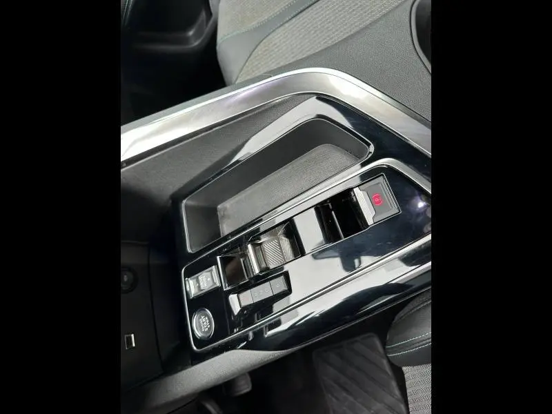 Vue rapprochée de la console centrale noire brillante du Peugeot 3008 Hybride Rechargeable 2024 avec commandes de boîte auto et frein à main électrique.