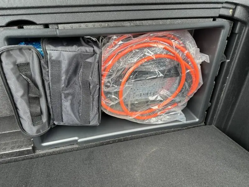Rangement dans le coffre du Peugeot 3008 hybride 2024 montrant un câble de recharge orange et une trousse noire.