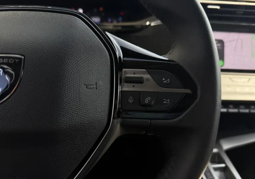 Gros plan sur la partie droite du volant noir de la Peugeot 308 SW 2025 avec commandes intégrées et écran tactile en arrière-plan.