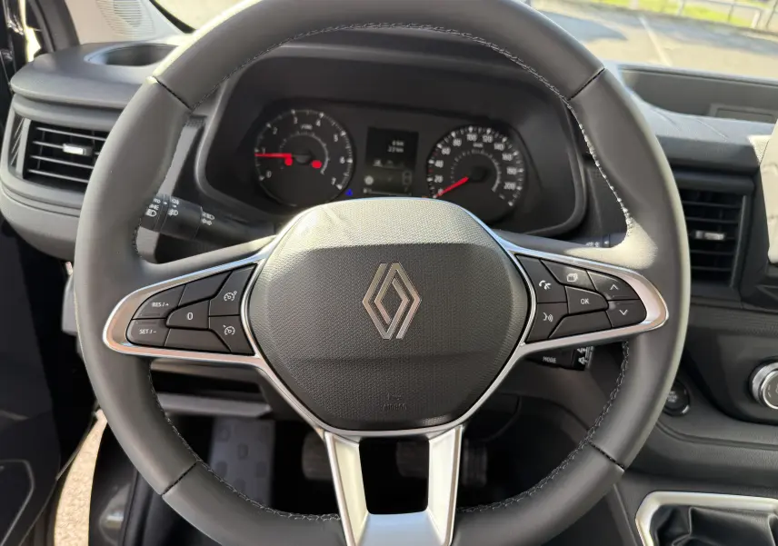 Vue rapprochée du volant noir du Renault Trafic Fourgon 2025 avec commandes intégrées et tableau de bord visible.