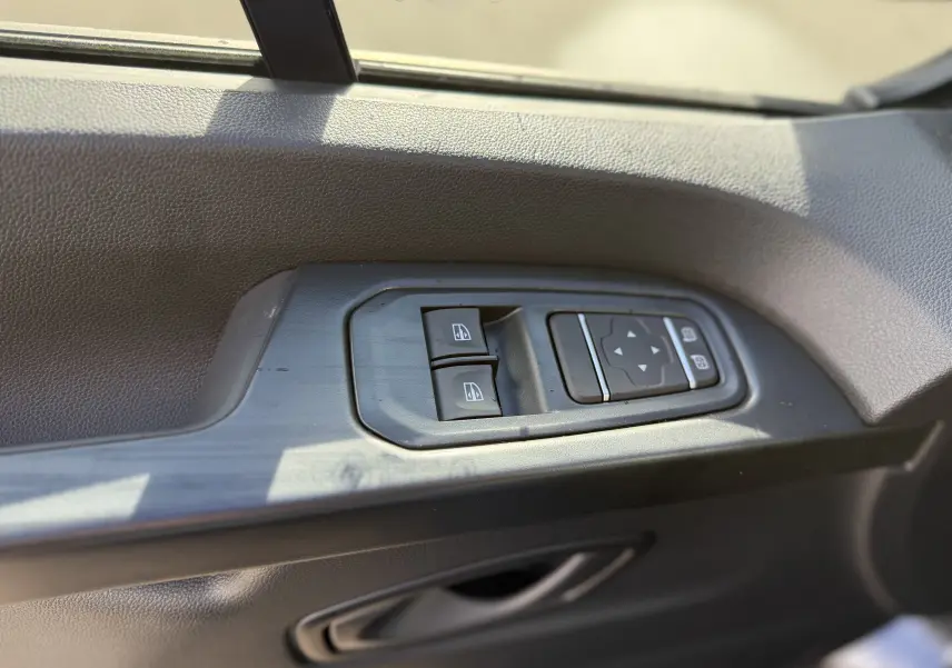 Gros plan sur les commandes de lève-vitres et réglage des rétroviseurs côté conducteur du Renault Trafic Fourgon noir crépuscule.