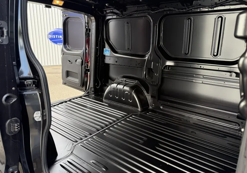 Intérieur du fourgon Renault Trafic noir crépuscule, vue depuis l'arrière avec porte latérale ouverte montrant la zone de chargement.