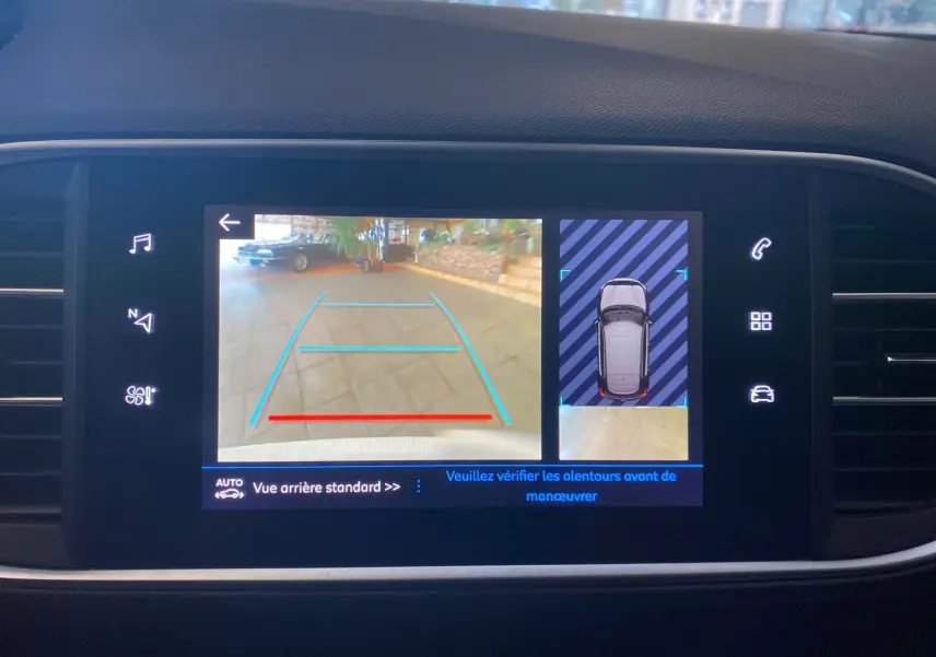 Écran tactile intérieur montrant la caméra de recul et l'aide au stationnement du Peugeot 308 blanc, version allure 2020.