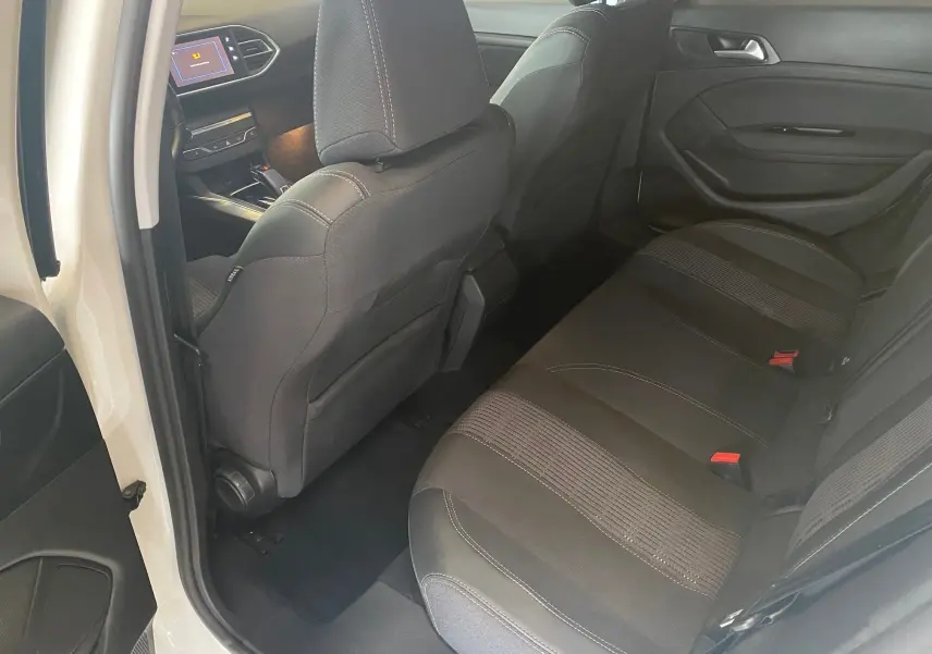 Vue intérieure arrière droite de la Peugeot 308 blanche 2020, sièges tissu noir avec coutures contrastées et tableau de bord visible.