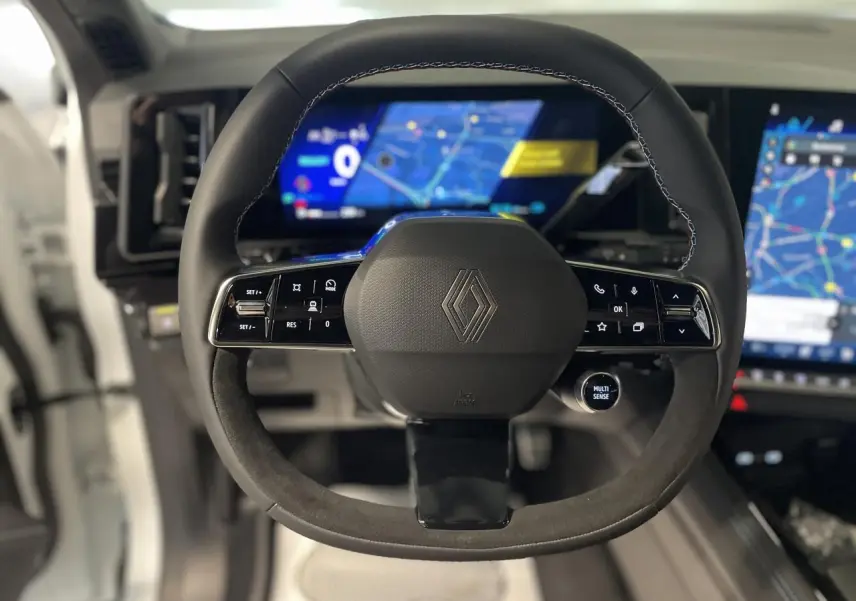 Volant Alcantara avec surpiqûres tricolores et logo Renault, tableau de bord numérique du Renault Austral 2025 visible en arrière-plan.