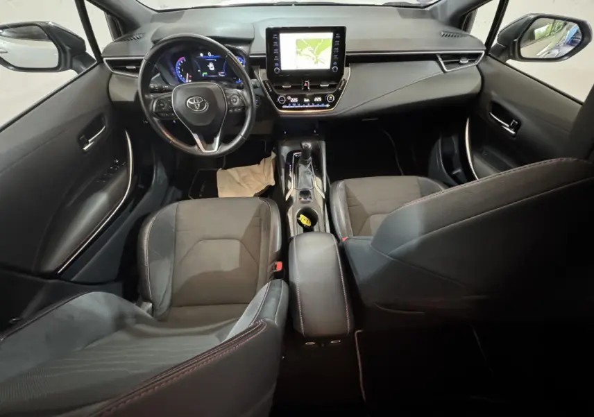 Intérieur noir de la Toyota Corolla Hybride 122h Collection 2021 vu de l'arrière, tableau de bord et écran tactile central visibles.