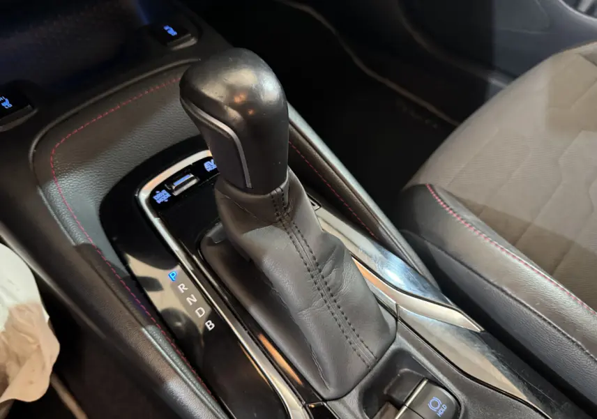 Le levier de vitesses automatique en cuir noir avec surpiqûres rouges dans une Toyota Corolla Hybride gris clair, vue intérieure rapprochée.