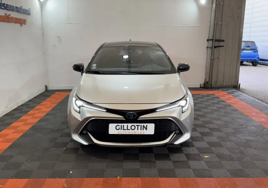 Toyota Corolla Hybride 122h Collection gris clair vue de face dans un garage avec sol à damiers noir et orange