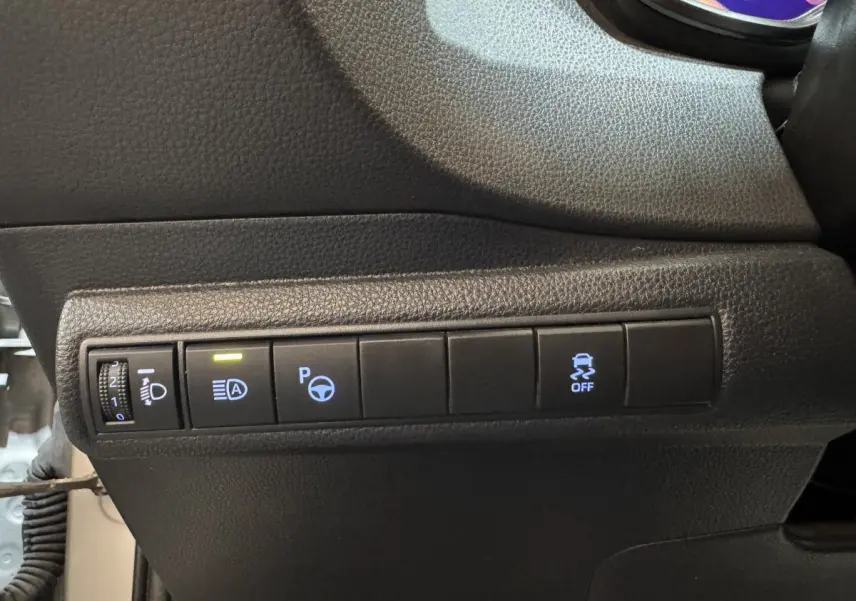 Panneau de commandes noires avec boutons d'assistance au stationnement et contrôle de phares dans une Toyota Corolla hybride gris clair 2021.