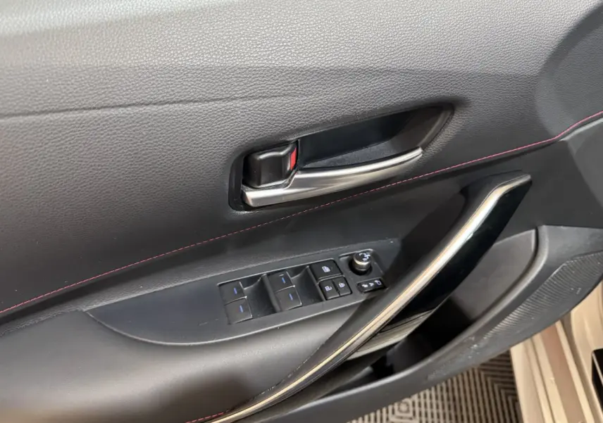 Gros plan sur la porte côté conducteur de la Toyota Corolla Hybride 122h Collection 2021 avec garniture noire et surpiqûres rouges.