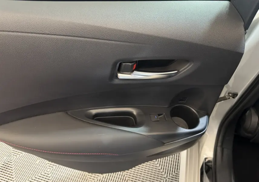 Vue rapprochée de la porte avant gauche gris clair de la Toyota Corolla Hybride 122h avec poignée intérieure chromée et accoudoir noir.