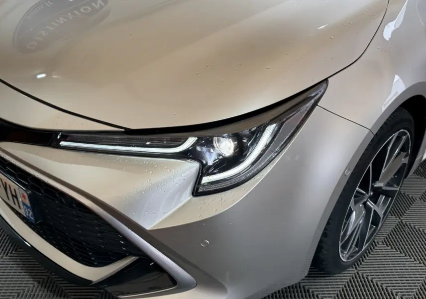 Gros plan sur l'avant droit gris clair d'une Toyota Corolla hybride 2021, mettant en valeur le phare LED et la jante alliage.