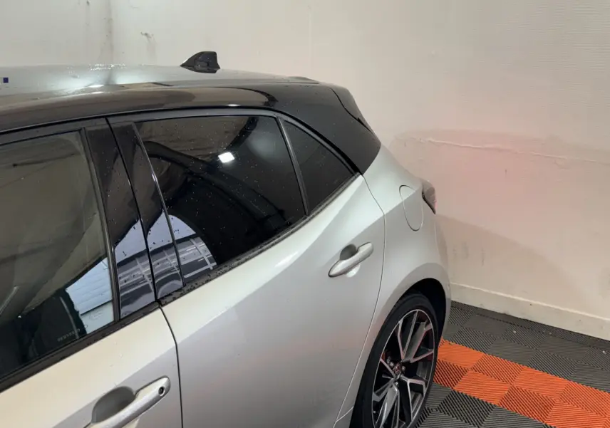 Vue côté arrière droit d'une Toyota Corolla hybride gris clair avec toit noir et jantes alliage sport.