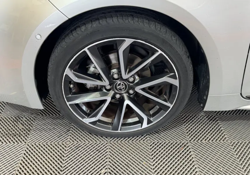 Gros plan sur la roue avant gauche de la Toyota Corolla hybride gris clair, avec jante alliage noire et argentée au design moderne.