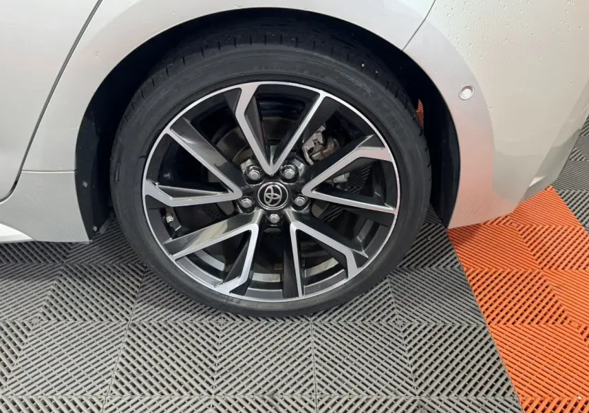 Gros plan sur la roue arrière droite gris clair d'une Toyota Corolla Hybride 122h Collection avec jante alliage noire et argentée.