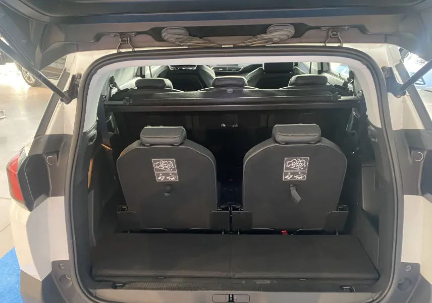 Coffre ouvert vue arrière d'un Peugeot 5008 blanc avec sièges rabattus et intérieur noir visible.