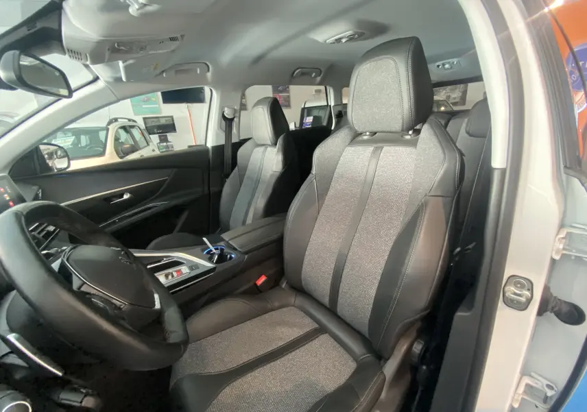 Intérieur du Peugeot 5008 blanc, vue côté conducteur, sièges en cuir et tissu gris avec tableau de bord moderne.