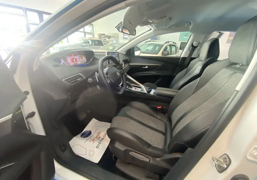 Vue intérieure côté conducteur du Peugeot 5008 blanc, mettant en valeur les sièges bi-matière gris et noir et le tableau de bord digital.