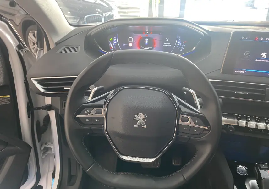 Vue intérieure centrée sur le volant cuir noir et le tableau de bord numérique du Peugeot 5008 blanc.