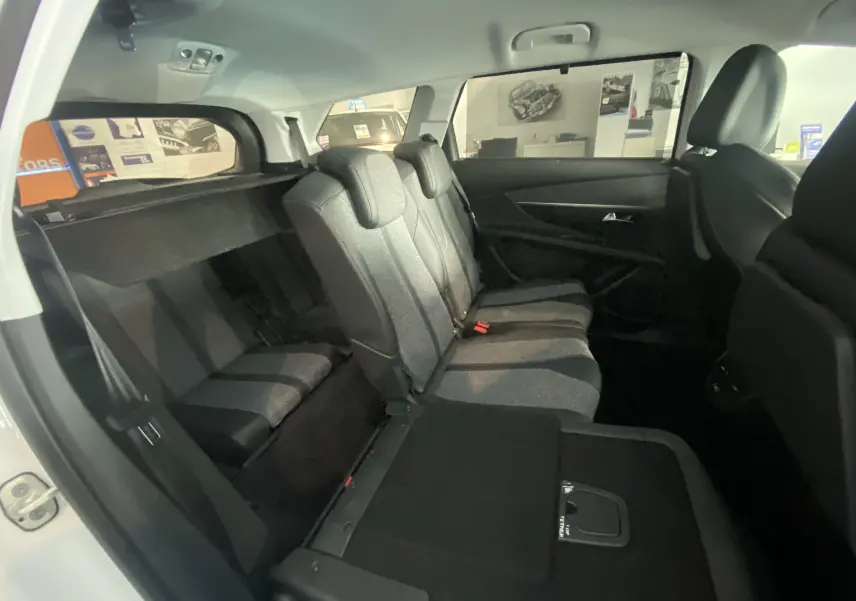 Vue intérieure côté droit du Peugeot 5008 blanc, montrant les sièges arrière en tissu gris avec une banquette partiellement rabattue.