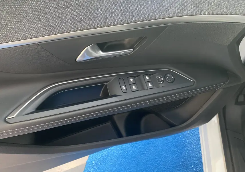 Vue rapprochée de la portière avant gauche noire du Peugeot 5008 blanc, avec commandes des vitres et poignée argentée.