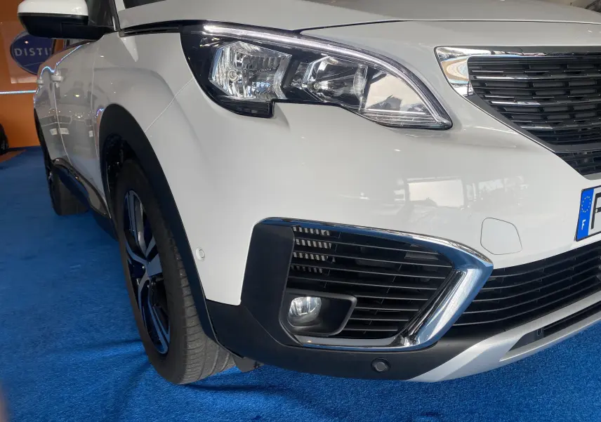 Gros plan sur l'avant droit blanc du Peugeot 5008 avec phares et calandre chromée visibles.