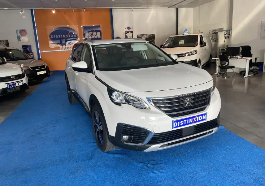 Peugeot 5008 blanc blanquise vue 3/4 avant droit avec attelage neuf dans un showroom intérieur.