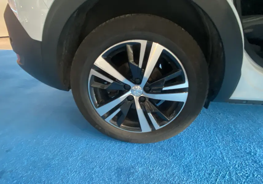 Gros plan sur la roue avant droite d'un Peugeot 5008 blanc Blanquise avec jante alliage bicolore.