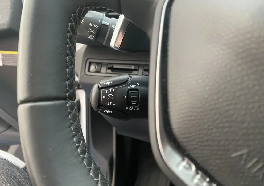 Gros plan sur la commande de régulateur de vitesse à gauche du volant d'un Peugeot 5008 blanc de 2019.