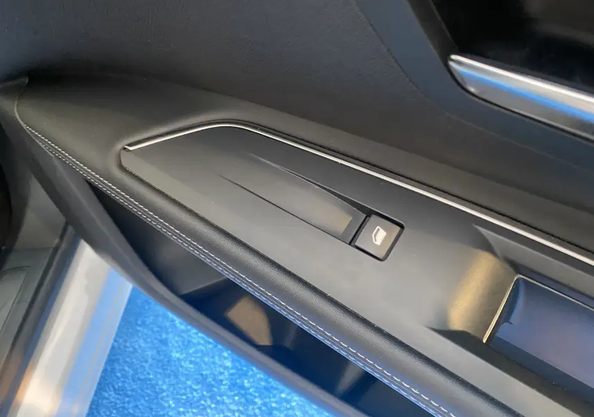 Gros plan sur la commande de lève-vitre côté conducteur du Peugeot 5008 blanc, avec surpiqûres blanches sur la garniture noire.