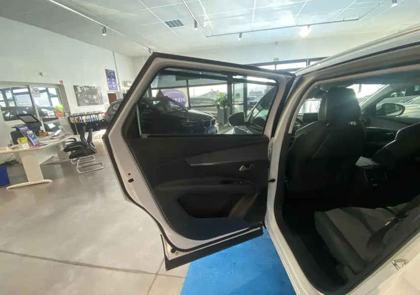 Porte arrière gauche ouverte d’un Peugeot 5008 blanc, montrant l’intérieur sombre et les sièges arrière dans un showroom.