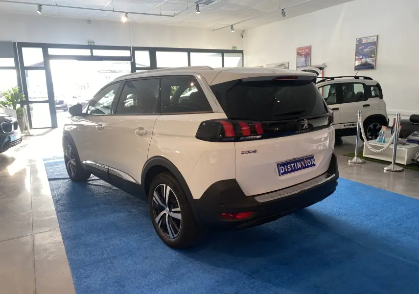 Peugeot 5008 blanc blanquise vu en 3/4 arrière droit dans un showroom avec attelage neuf visible.