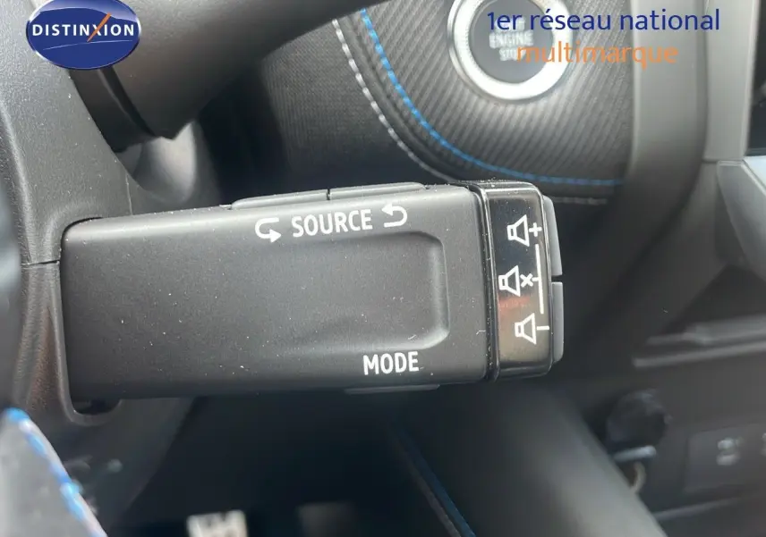 Commande au volant avec réglage du volume et source audio sur Renault Captur E-Tech hybride 2025, intérieur noir avec surpiqûres bleues.
