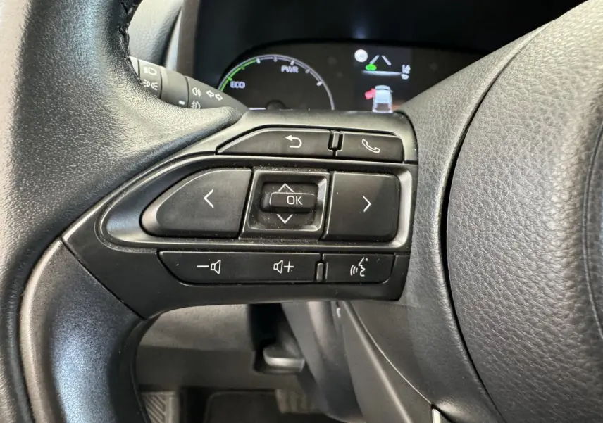 Gros plan sur les commandes gauche du volant cuir noir de la Toyota Yaris Hybride 2022 avec affichage digital en arrière-plan.
