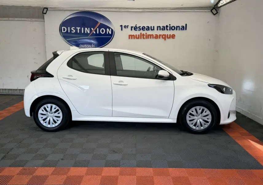 Profil côté gauche d'une Toyota Yaris hybride blanche 2022, avec jantes standard et toit noir contrasté en arrière-plan intérieur.