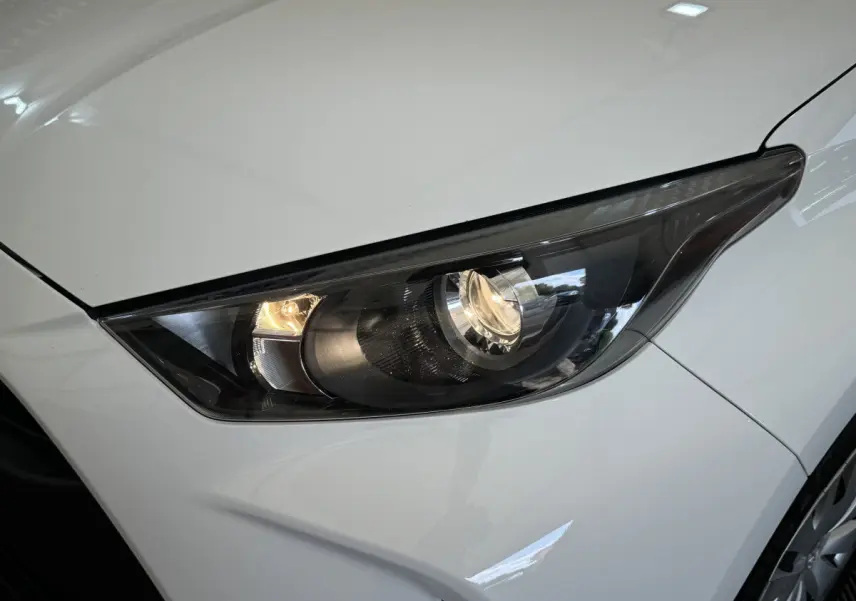 Gros plan sur le phare avant droit allumé d'une Toyota Yaris hybride blanche 2022, avec carrosserie lisse et jante visible.