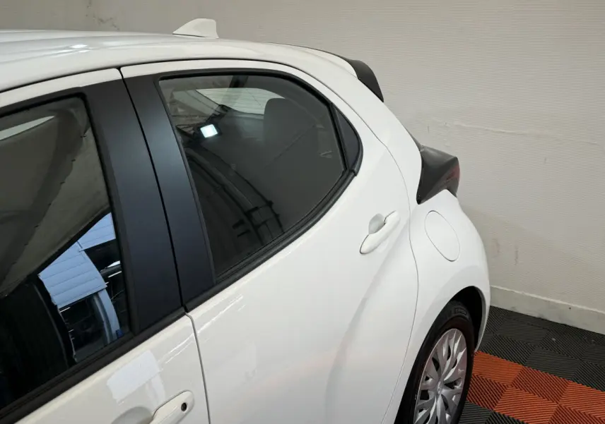 Vue latérale arrière droite de la Toyota Yaris hybride blanche 2022, soulignant la porte et l'aile arrière.