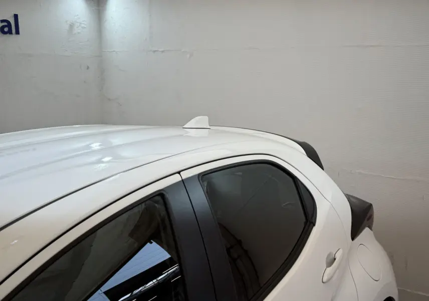 Vue latérale côté droit d'une Toyota Yaris hybride blanche avec antenne requin sur le toit et vitres teintées