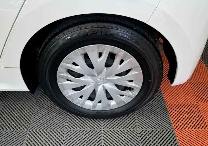 Gros plan sur la roue arrière droite blanche de la Toyota Yaris Hybride 116h avec enjoliveur argenté et logo Toyota visible.
