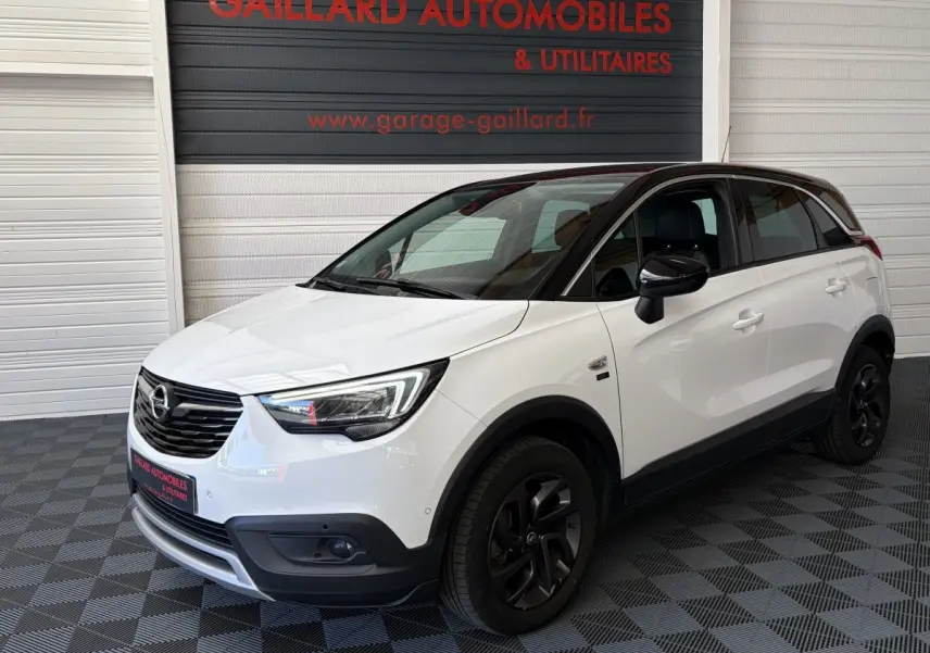 Vue 3/4 avant droite d'un Opel Crossland blanc 2021 avec toit noir et jantes noires dans un showroom.
