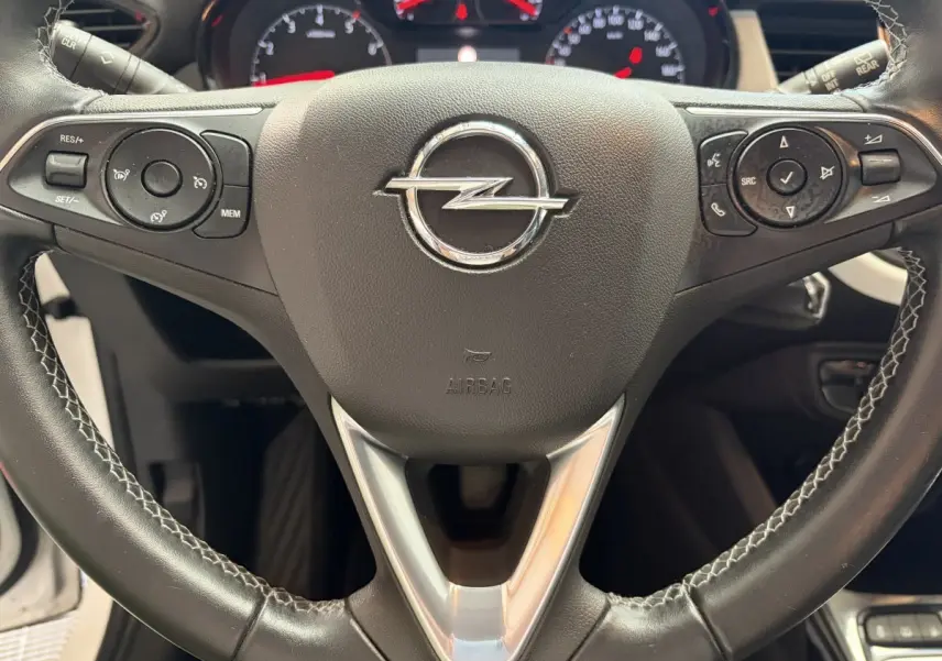 Gros plan sur le volant cuir et alu de l’Opel Crossland blanc, avec commandes multifonctions et logo central visible.