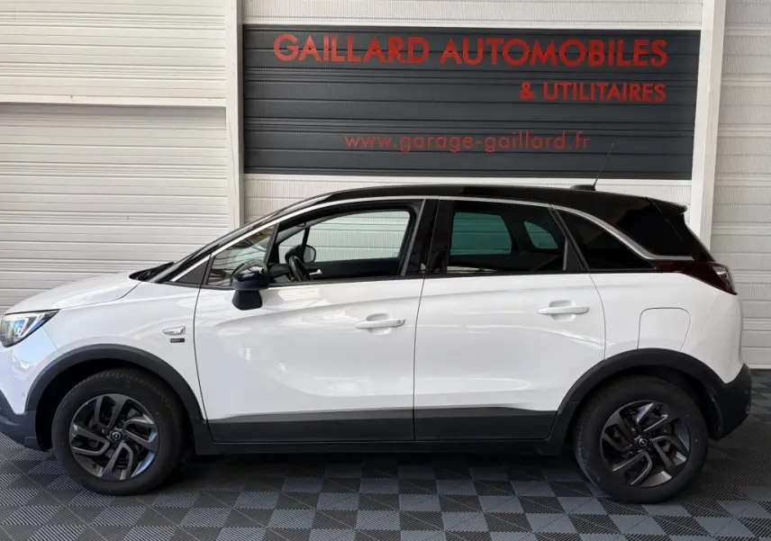 Opel Crossland blanc vue de profil côté gauche, toit noir contrasté et jantes foncées, en intérieur de garage.