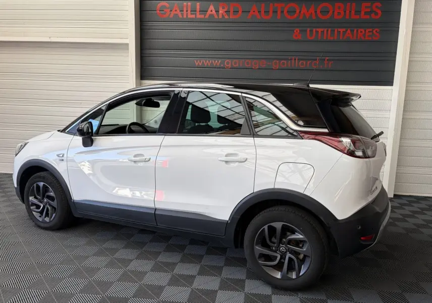 Vue de profil côté gauche d'un Opel Crossland blanc avec toit noir et jantes foncées dans un garage.