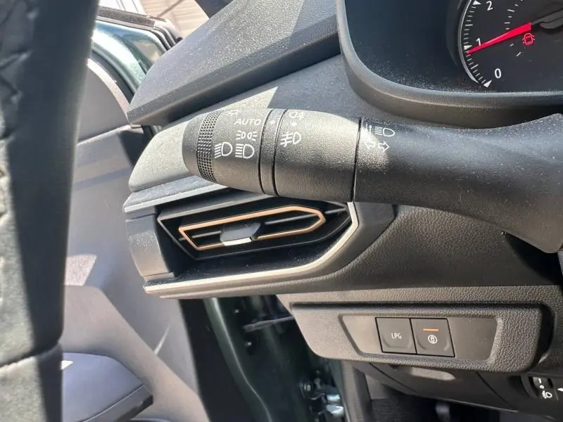Détail intérieur côté gauche du tableau de bord vert cèdre métallisé avec commande des phares et bouton GPL sur Dacia Sandero 2025.