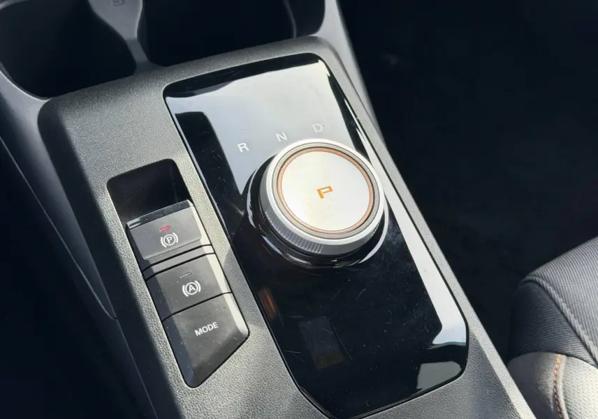 Gros plan sur la console centrale noire brillante avec sélecteur rotatif de boîte auto et boutons mode et frein à main MG3 2025.