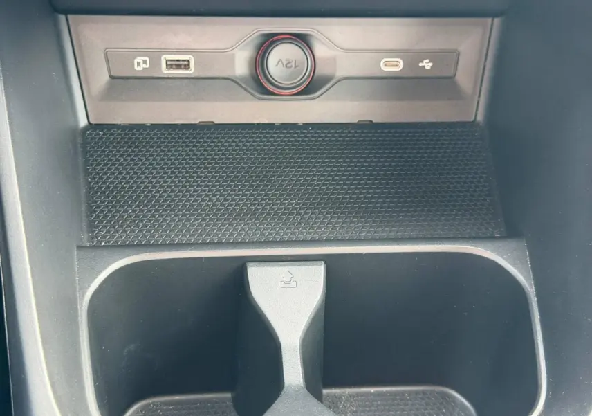 Gros plan sur la console centrale noire du MG3 1.5 Hybrid+ avec prise 12V, port USB et rangement intégré.