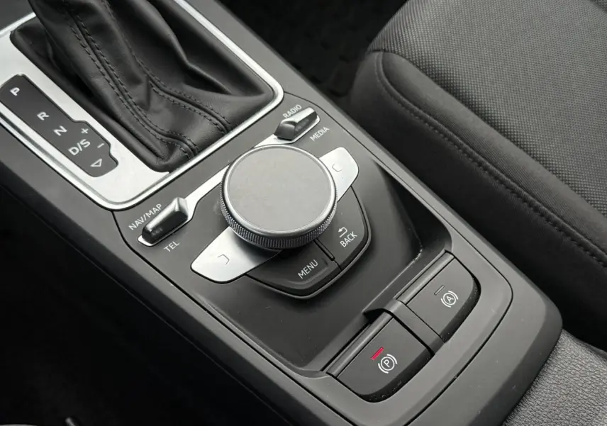 Gros plan sur la console centrale noire de l'Audi Q2 35 TFSI 2023, montrant la molette MMI et le levier de vitesses automatique.