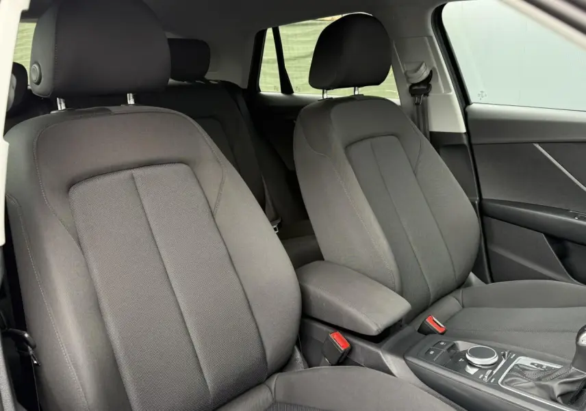 Intérieur de l'Audi Q2 35 TFSI S-Line 2023 montrant les sièges avant en tissu gris et la console centrale.