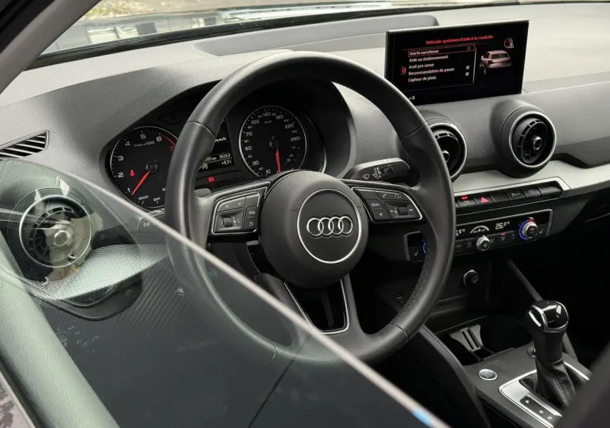 Vue intérieure côté conducteur de l'Audi Q2 35 TFSI 150 S-Tronic S-Line 2023, tableau de bord et volant multifonction.