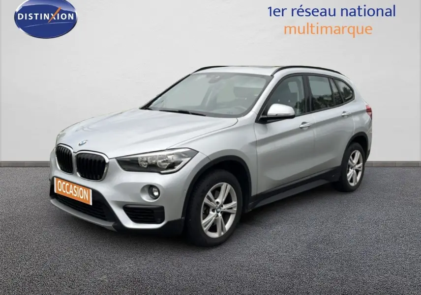 BMW X1 18i gris argent métal en 3/4 avant droit, avec jantes alliage et calandre noire distinctive.